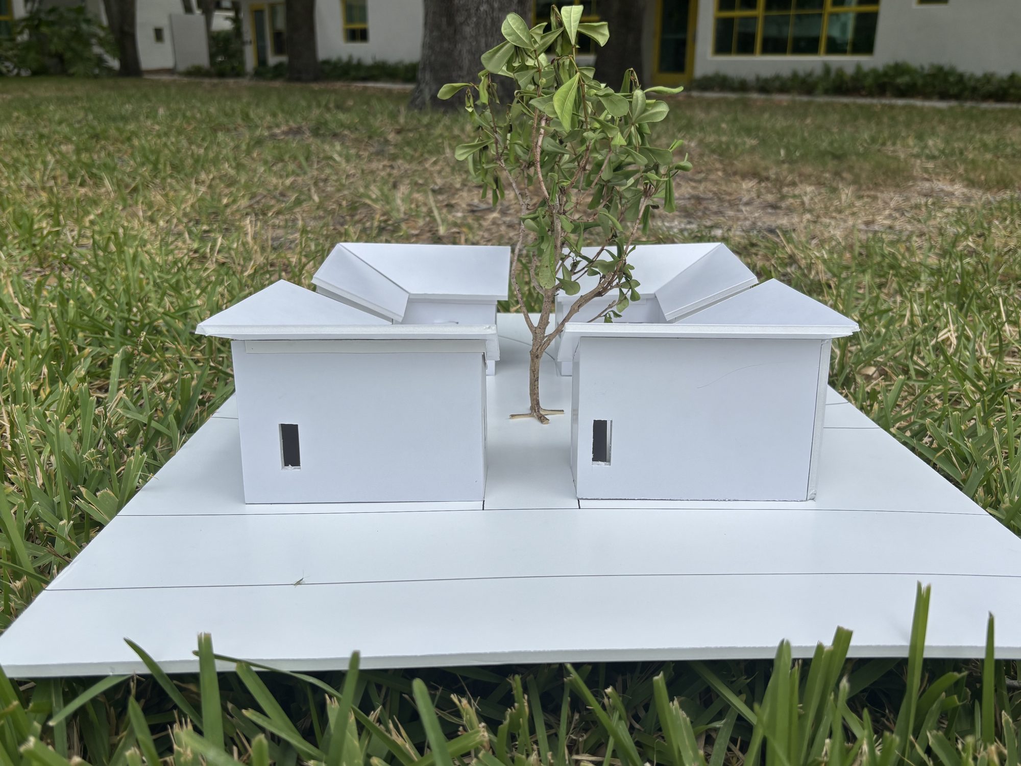 The meditation space model photographed on grass: gabled pavilions around a courtyard tree