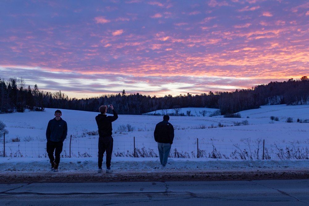 Three figures against a pink winter sunset over snow